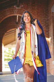 Close-up of Diana walking under the Old Main archway, looking joyful as she holds her gown over her shoulder.