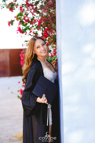 Portrait of Brenda smiling while holding her graduation cap, showcasing happiness and achievement.