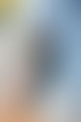 Brenda smiling radiantly while leaning against a blue wall, wearing her graduation cap and holding her gown over one shoulder.