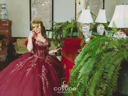 Close-up of Luciana wearing a gold masquerade mask and jeweled gown among vintage decor.