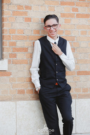 Smiling Israel straightening his tie while leaning on a brick wall during his stylish senior session in Tucson.