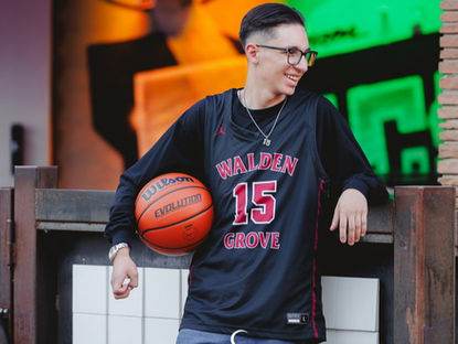 Israel leaning on an urban railing, clutching a Wilson basketball while smiling in his WaldenāÆGroveāÆ#15 jerseyādowntown Tucson senior photo.