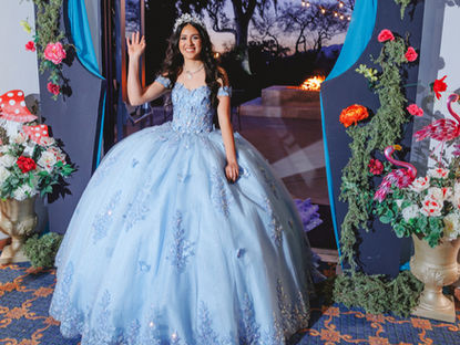 Grand entrance moment as Aurelise waves and walks through the decorated Alice in Wonderland-themed arch with indoor sparklers.