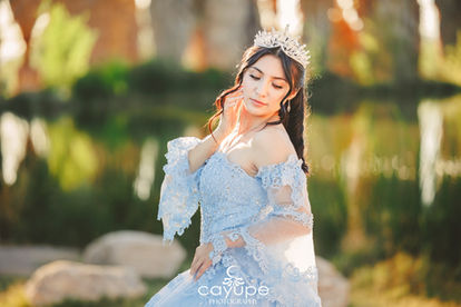 Dezeray smiling while sitting on a rock near the lake, pairing cowboy boots with her pastel blue dress.