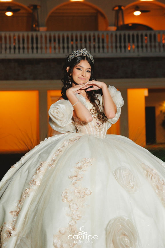 Close nighttime portrait of Brianna framing her face with hands beneath twinkling terrace lights, highlighting her tiara at Omni Tucson.