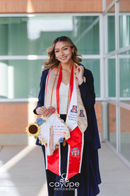 Cassandra wearing her graduation gown and red stole, holding a sunflower and decorated cap at the University of Arizona.