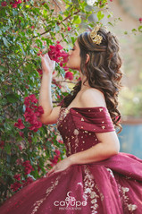 Profile of Luciana smelling bright bougainvillea, gold crown and burgundy dress against a Tucson garden backdrop.