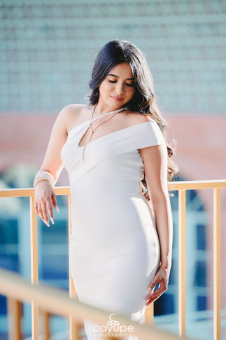 Elegant young woman in a white dress looking down gracefully while standing by a yellow railing.