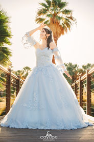 Dezeray leaning on a railing, with natural light emphasizing her face and pastel blue dress.