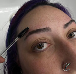 Woman brushing her eyebrow with a spoolie, purple hair, nose ring.