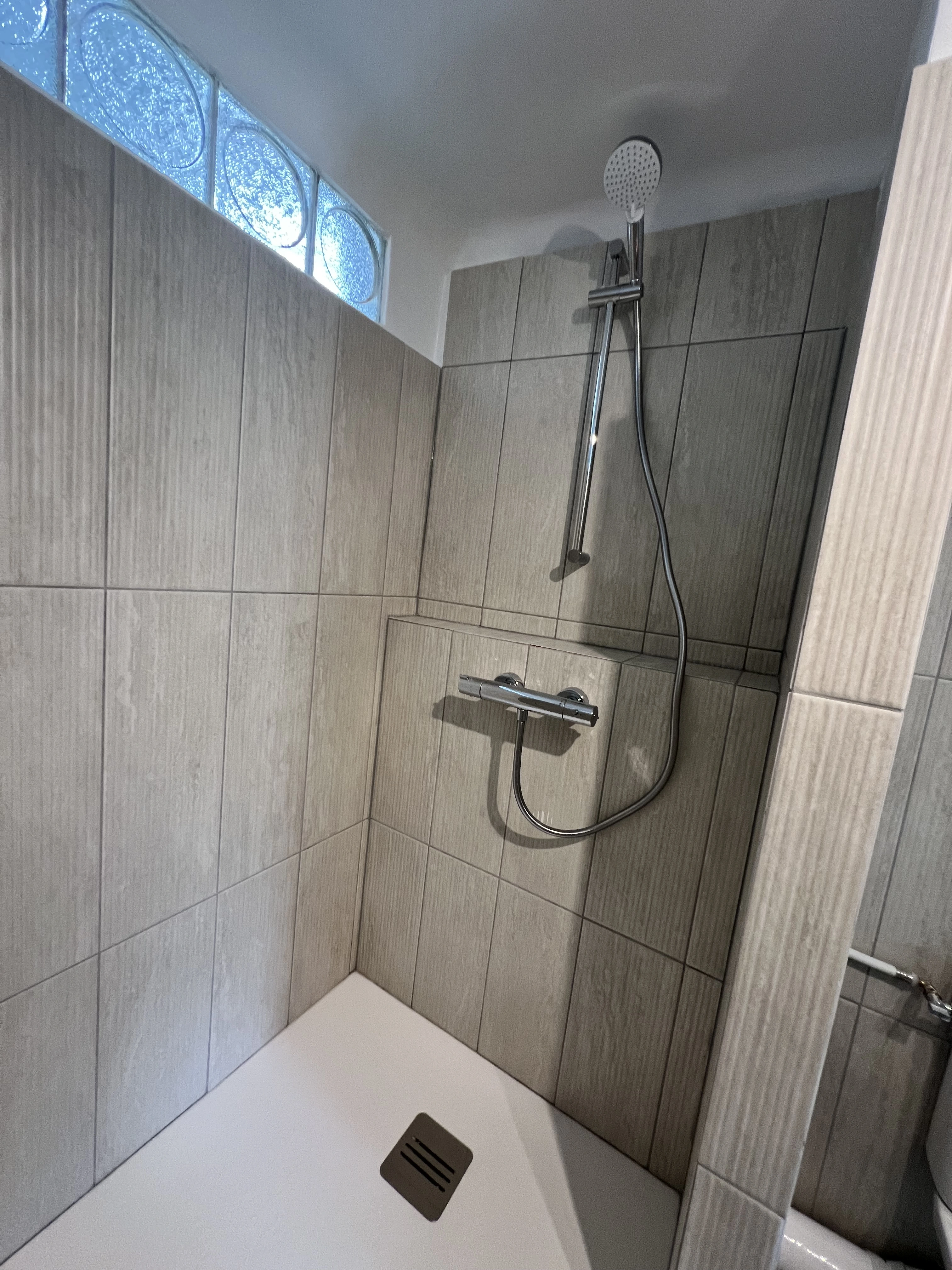 Pose de carrelage travertin retaillé et faïence ondulée pour une salle de bain lumineuse et harmonieuse.