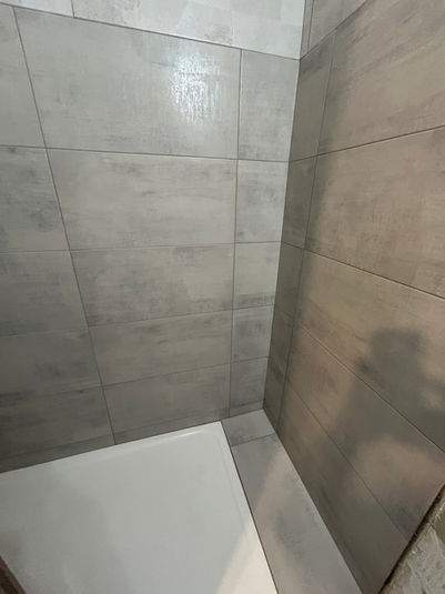Douche en angle avec carrelage gris effet béton et receveur blanc