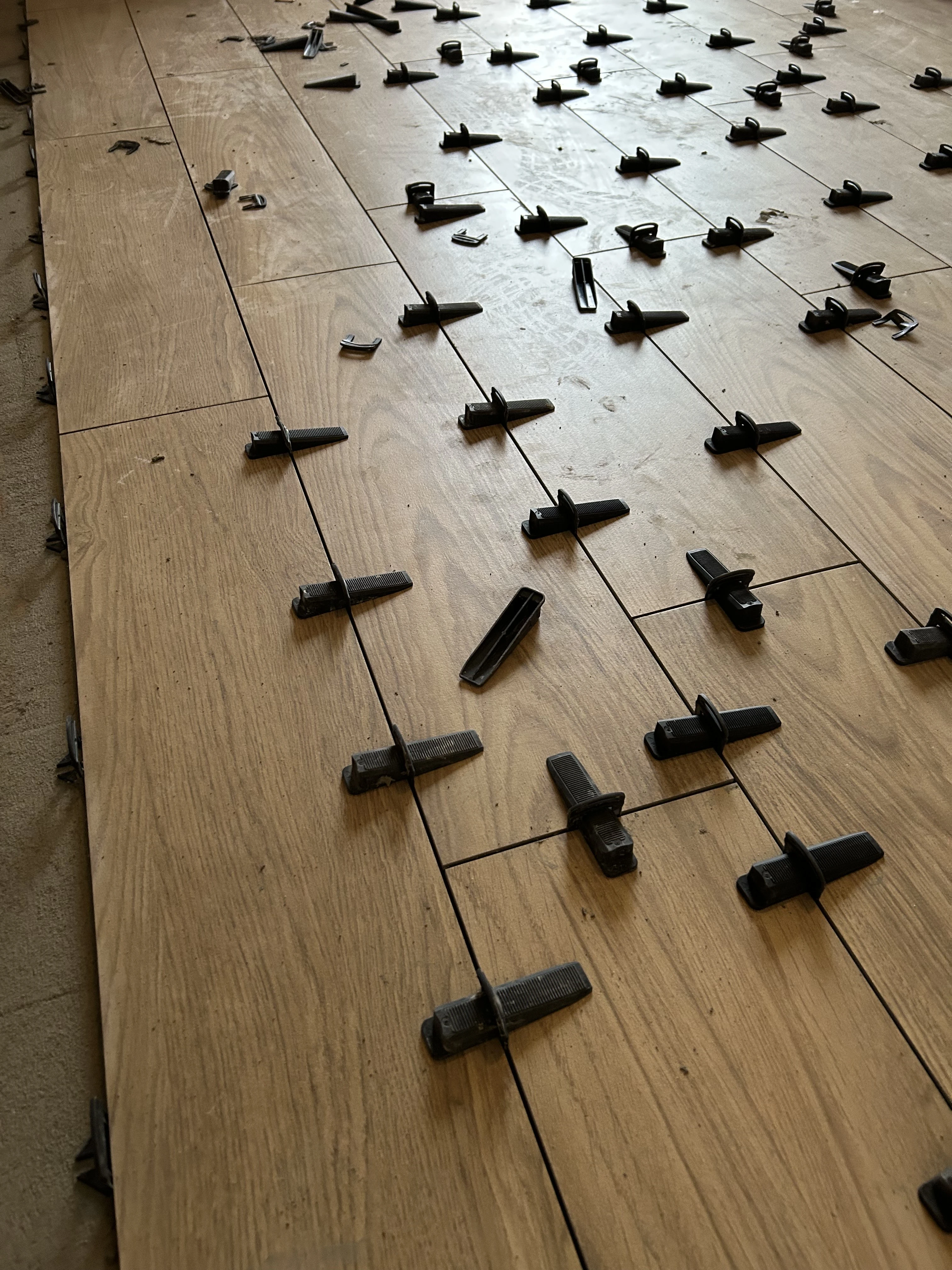 Pose d’un carrelage aspect bois avec croisillons et cales de nivellement pour une finition impeccable.