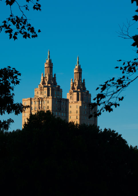 Two illuminated towers framed by dark tree silhouettes against a bright blue sky. The architectural details stand out in the golden light of the setting sun.