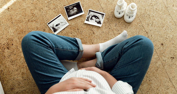 top view of a pregnant woman sitting on the floor hugging her belly and looking at an ultr