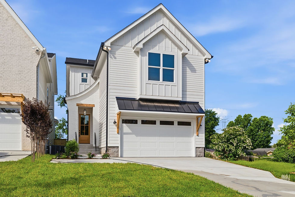 Modern white two-story house with black metal roof accents, double garage, front porch with wood trim, green lawn, neighboring houses, and blue sky, wide landscape aspect ratio.