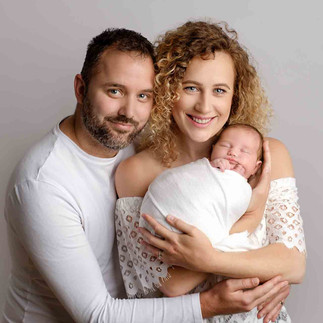 new parents hold their newborn baby dressed in white