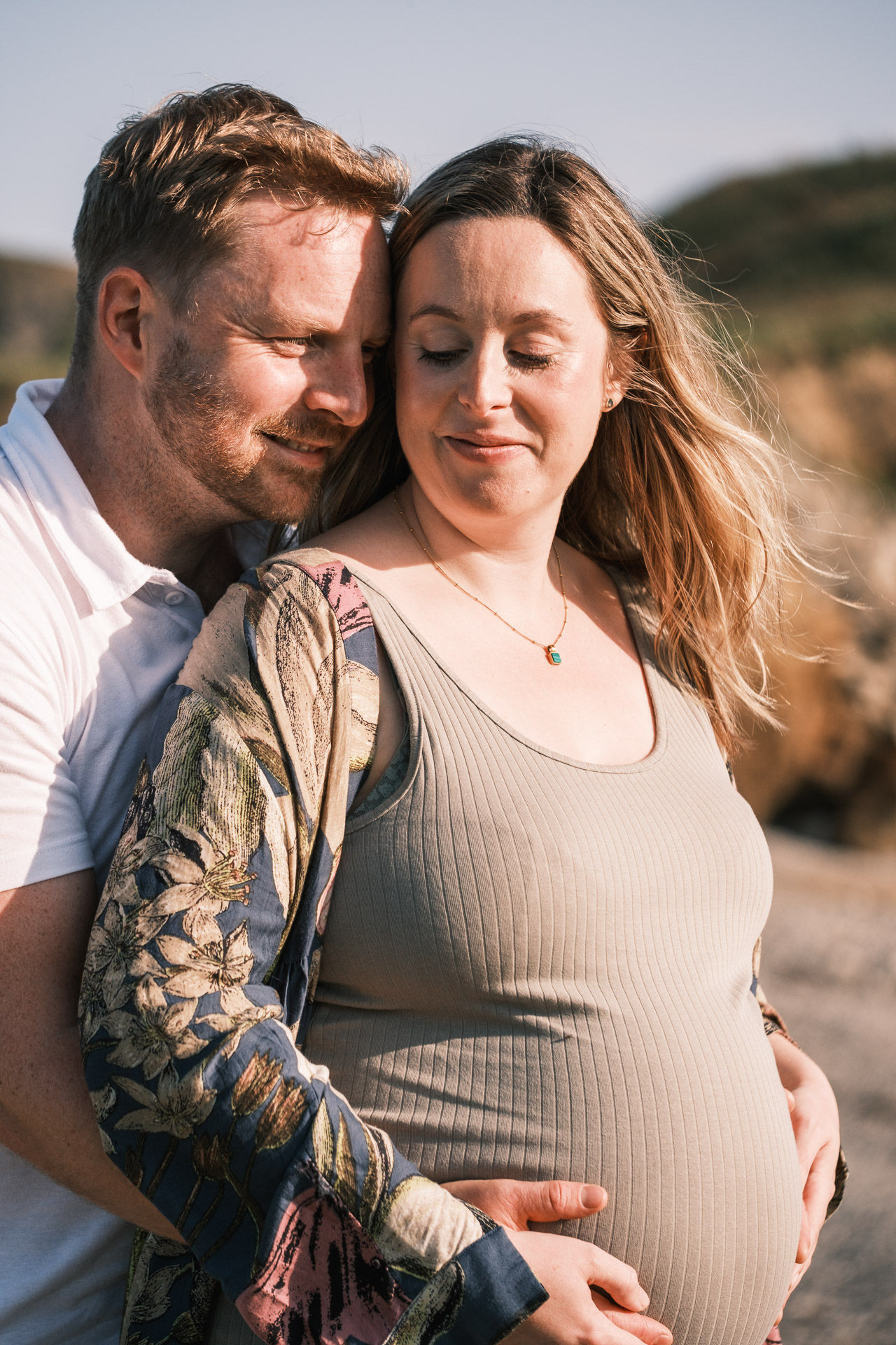 a man and pregnant lady embrace on the beach