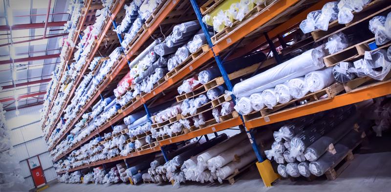 Large scale industrial warehouse with rows of premium fabric rolls on steel shelving.
