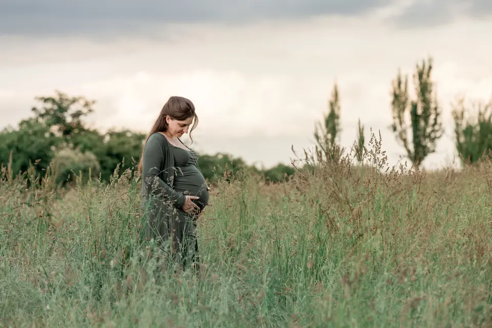 photographie d'une femme enceinte en extérieur dans un parc à la rochelle. la femme regarde tendrement son ventre en le caressant. elle a une robe verte et est placée dans les hautes herbes