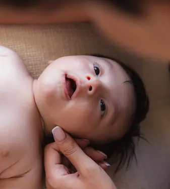 photographie d'un bébé qui regardent sa maman avec amour, on ne distingue pas le visage de la mère mais elle lui caresse la joue, le bébé a 2 mois