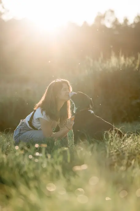 photographie d'un chien et sa maitresse en extérieur à la rochelle au couché du soleil dans un parc. le chien lui fait un bisous sur la joue