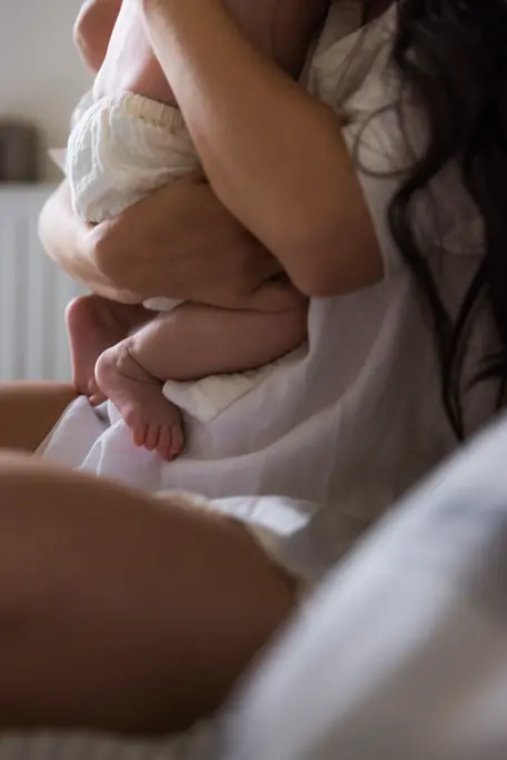 photo d'une maman et son bébé sur le lit dans la chambre. on ne distingue seulement que les pieds et le corps du bébé, la maman le sert fort dans ses bras