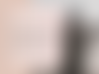 A woman stands on a beach facing the rocking shoreline. She is wearing a jacket with a leopard print scarf and a light grey knit hat.