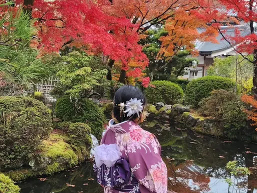 Creadora de Takassandra con kimono frente a un estanque rodeado de árboles con colores otoñales en Japón