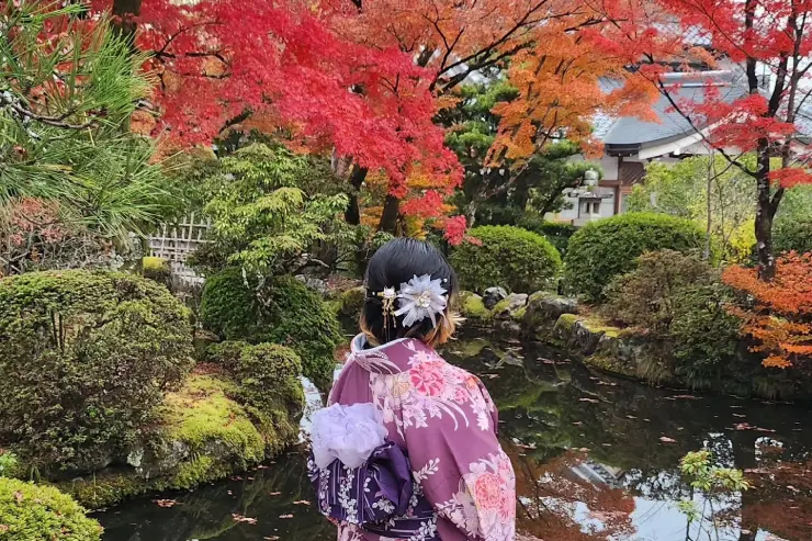 Creadora de Takassandra con kimono frente a un estanque rodeado de árboles con colores otoñales en Japón