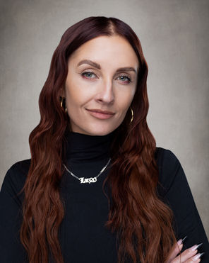 Headshot of Larissa Denton, 20-30 years old, with long red hair and green eyes wearing a black turtleneck and simple gold jewelry.