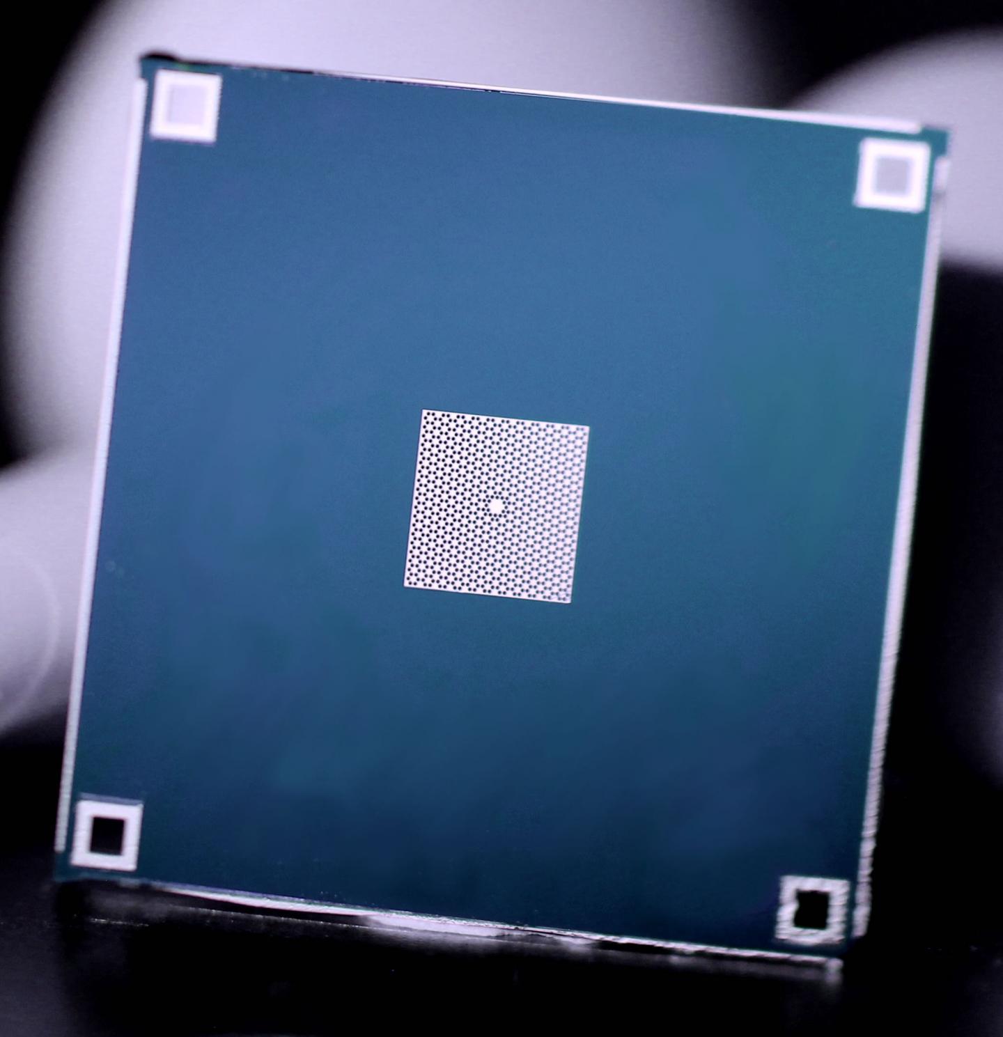 A thin silicon nitride membrane (white) is stretched tight across a silicon frame (blue). The membrane contains a pattern of holes, with one small island in the center, whose vibrations are measured in the experiment. @ Ola Joensen