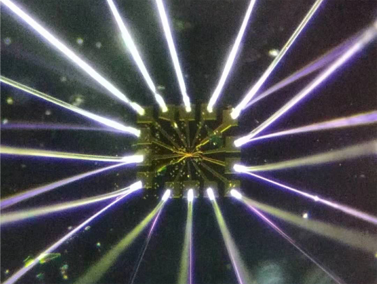 An optical image of the graphene device (shown above as a square gold pad) on a silicon dioxide/silicon chip. Shining metal wires are connected to gold electrodes for electrical measurement. The tiny graphene device has a length and width of just one-tenth of a millimeter. @ Guorui Chen/Berkeley Lab