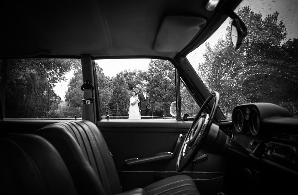 Brautpaar sitzt im Oldtimer und blickt durch das Fenster während der Hochzeitsfahrt