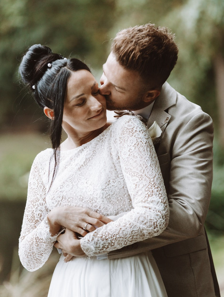 Braut lehnt sich liebevoll an den Bräutigam in inniger Umarmung
