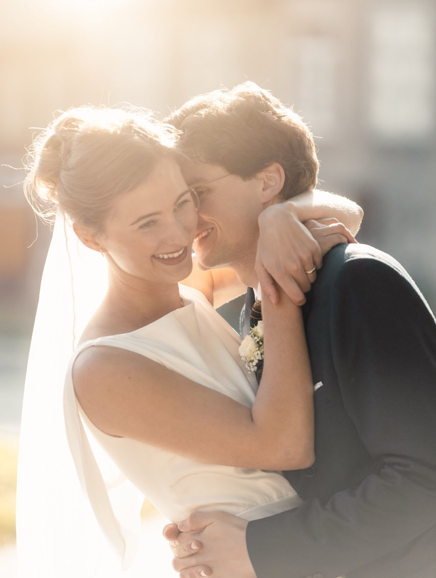 Brautpaar lacht glücklich in enger Umarmung bei Sonnenlicht