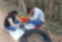 Two technicians working on fiber optic cable installation outdoors, with tools and cable rolls on the ground, in a rural setting.