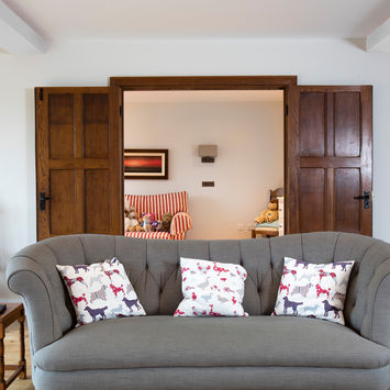 Grey sofa with patterned pillows in a living room; open doors.