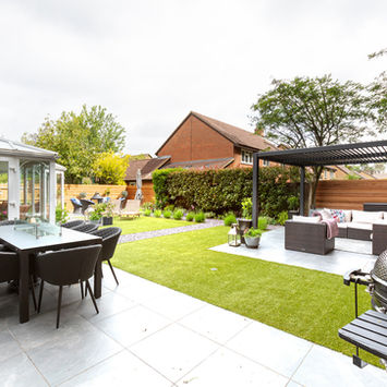 Outdoor patio with dining table and seating, green grass, and garden landscape.