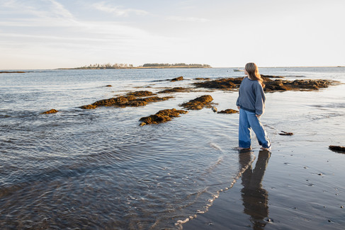 Girl walking on beach at sunset looking at towards the ocean wearning jeans and sweater