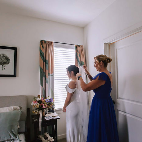 Bride in white gown getting hair styled by woman in blue.