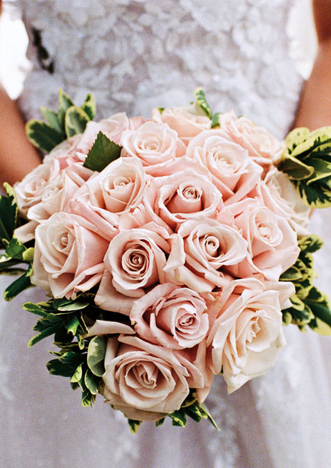 Bride in white dress holding a bouquet of light pink roses.