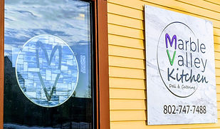 Sign saying "Marble Valley Kitchen, Deli & Catering" 802-747-7488 and stained glass piece with a purple M and green V that form a heart