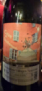 Wine bottle with label "Cave de Clochemerle" on a coral background, featuring shutters and a dome. Text includes 2025 Beaujolais-Villages Nouveau.