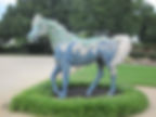 A horse sculpture encrusted with an oceanic mural stands in a flowerbed.