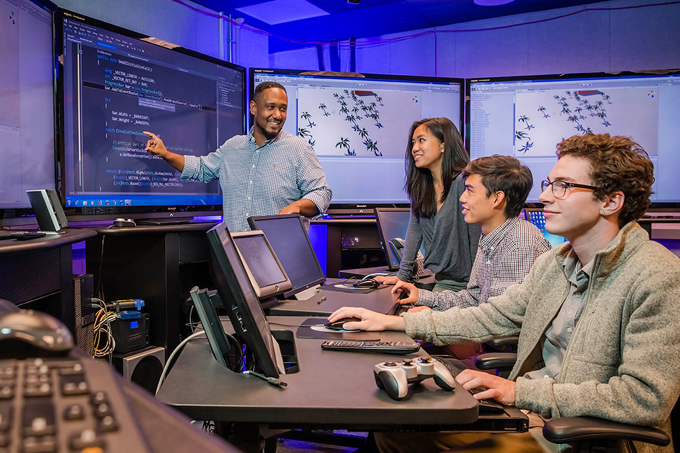 Four people in a tech lab, focused on a presentation. A man points at code on a large screen. Other screens show graphics. Mood is engaged.