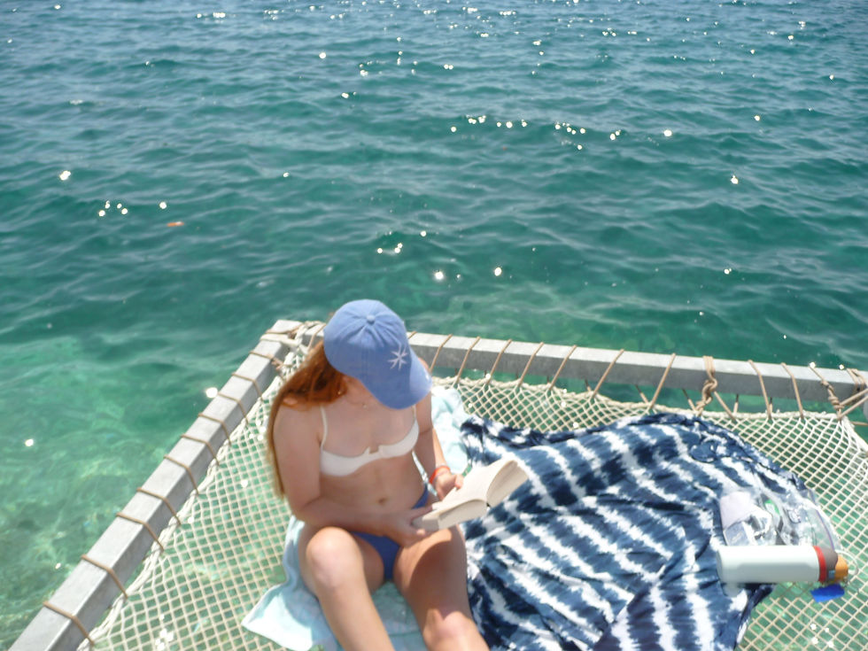 Woman reading book suspended in net over blue water