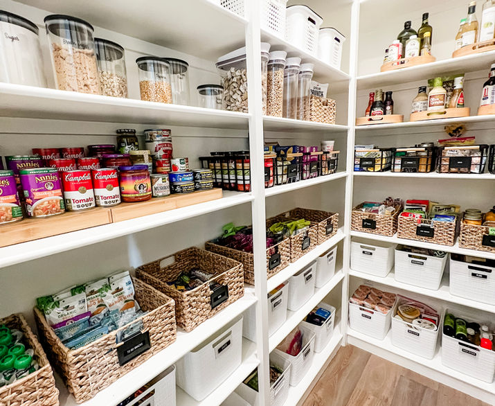 A large walk-in organized pantry with white shelves and food organized in white, black, and wood tone bins