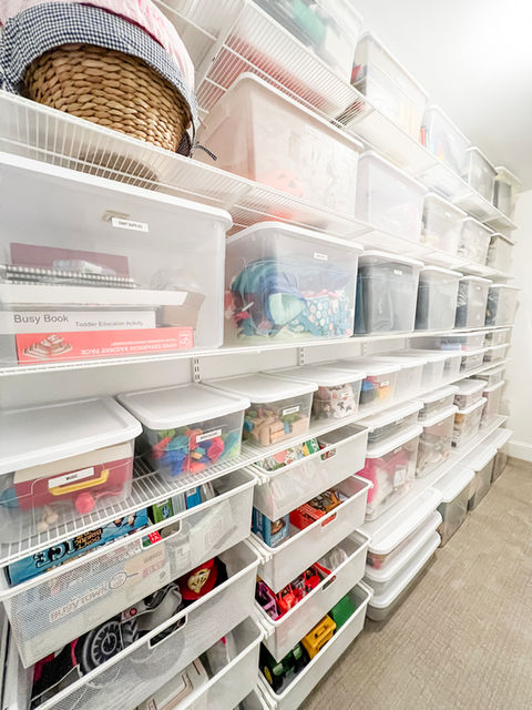 A long narrow storage room with white Elfa shelves along one side with belongings stored in clear storage totes with white lids.
