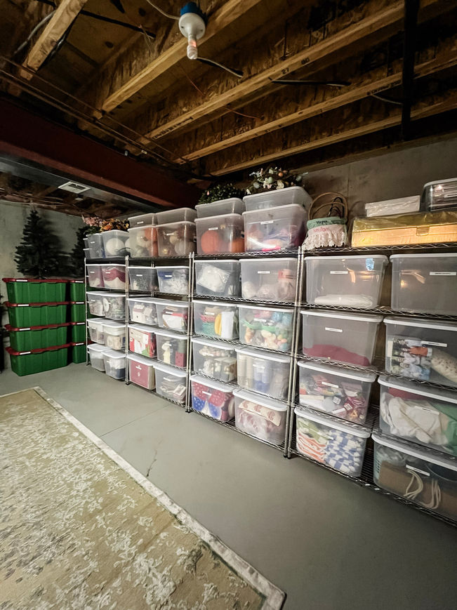 A dark basement with concrete floors, exposed ceilings, and metal racks lining the wall with consistent storage totes that are neatly labeled